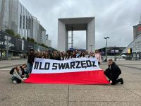Uczestnicy wycieczki do Paryża stojący przed Łukiem w dzielnicy III Tysiąclecia trzymając flagę Polski z napisem II LO...