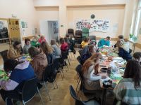 Uczniowie wraz z seniorami siedzą przy stole i wykonują kartki świąteczne
